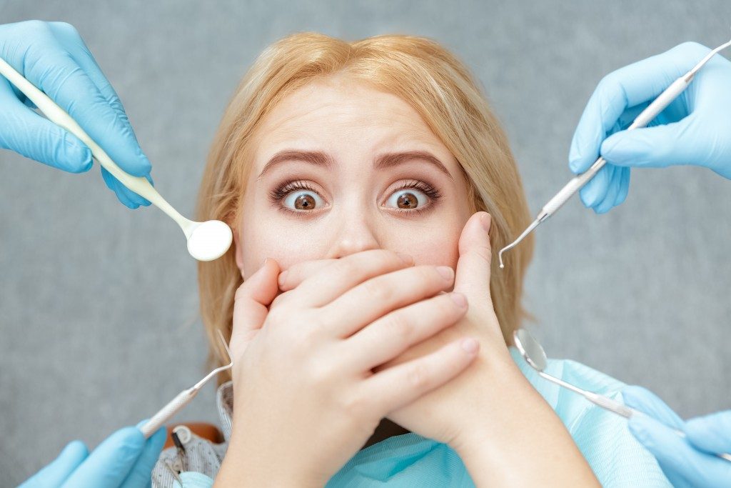 Closeup shot of a terrified female covering her mouth with both hands at the dentist appointment