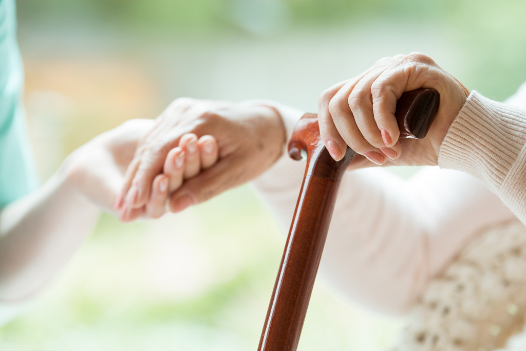 A senior holding a wooden cane while a healthcare worker holds their hands